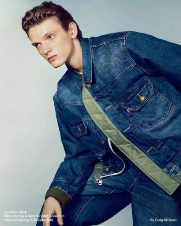 Fashion editorial of a young adult male model wearing a denim jacket and jeans against a neutral backdrop. The image showcases the clothing texture.