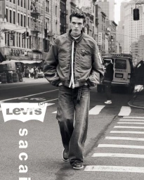 Monochrome street fashion campaign image featuring a male model walking across a city street wearing a bomber jacket and relaxed jeans.