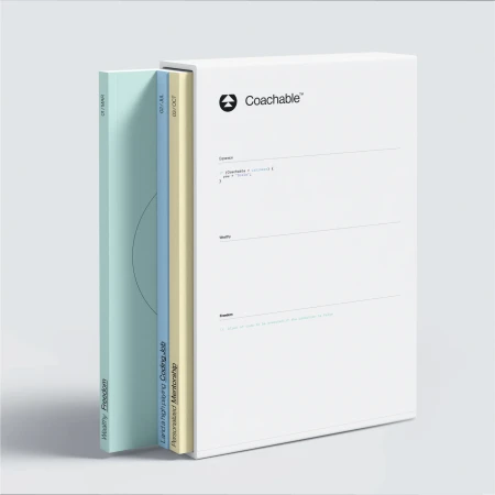 Coachable educational books in various colors, spines facing the camera, with the words 'Wealthy Freedom' and 'Personalized Mentorship'.