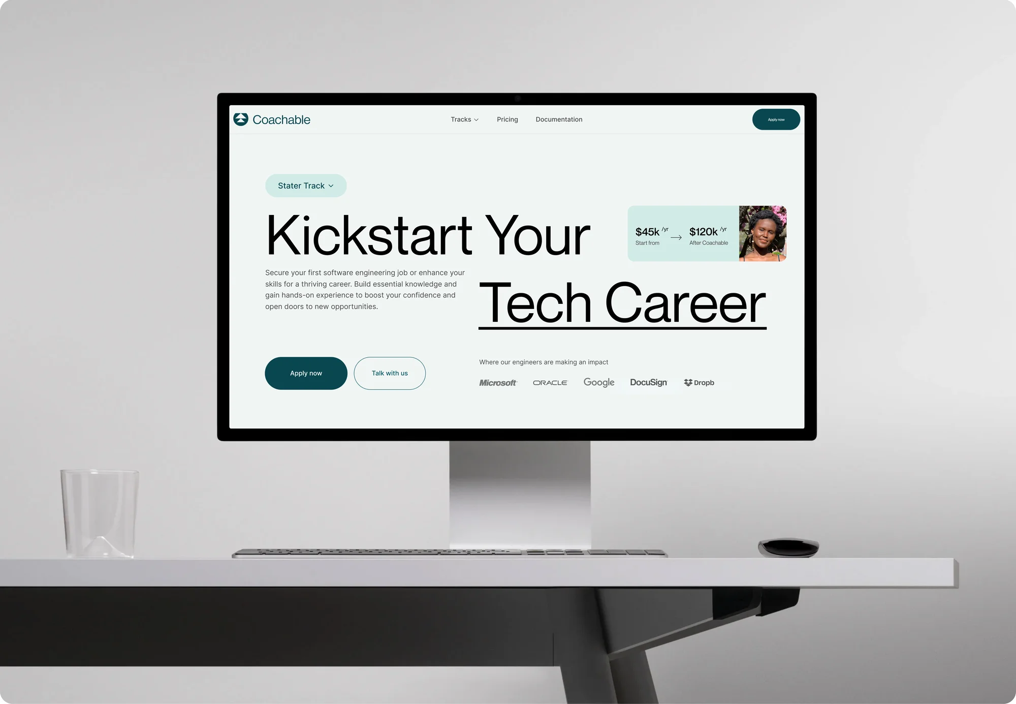 Computer monitor displays Coachable website on a white desk with a minimalist office aesthetic. The screen features text and interface.