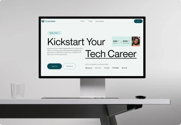 Desktop computer displaying the Coachable brand website interface on a clean white desk against a gradient grey background