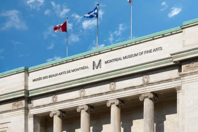Montreal Museum of Fine Arts architectural detail with facade and three flags including Canada, Scotland, and unidentified flag against blue sky.