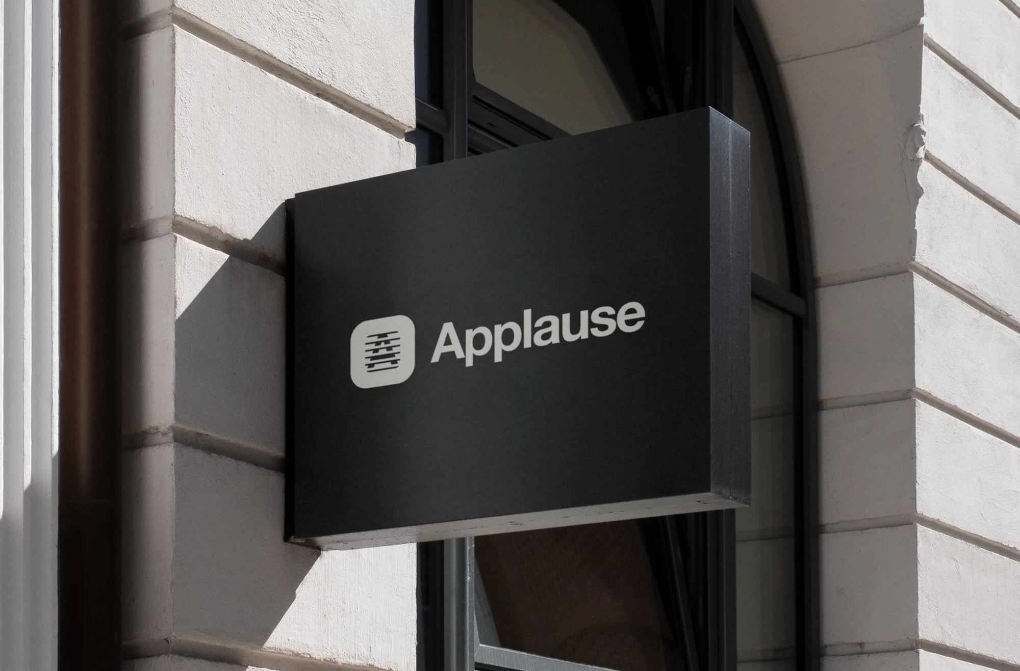 Close-up of a black sign with the white 'Applause' logo attached to a building, indicating a business or location.
