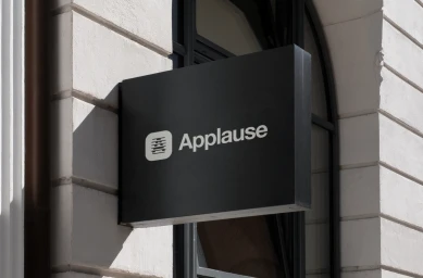 Black rectangular sign with white Applause branding mounted on a light-colored classical architectural wall