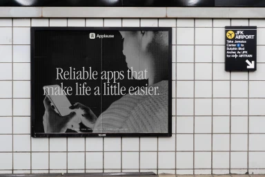 Black and white advertisement poster for Applause displayed on a tiled wall at JFK Airport subway station