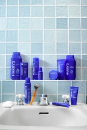 Harry's blue grooming products and a razor arranged on a bathroom sink against light blue tiled wall