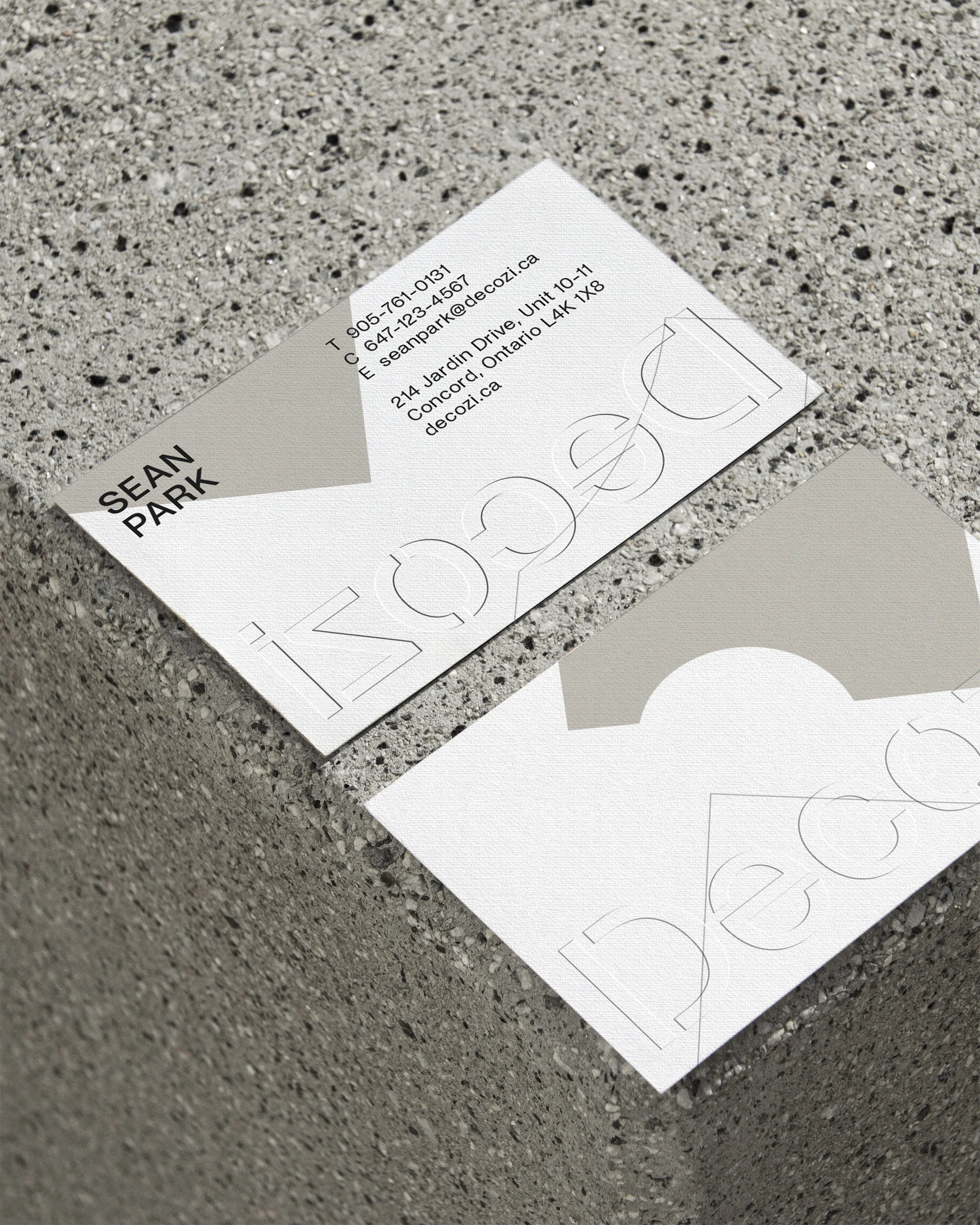 Two light grey and white business cards with embossed text sit on a textured grey surface, arranged diagonally in the composition.