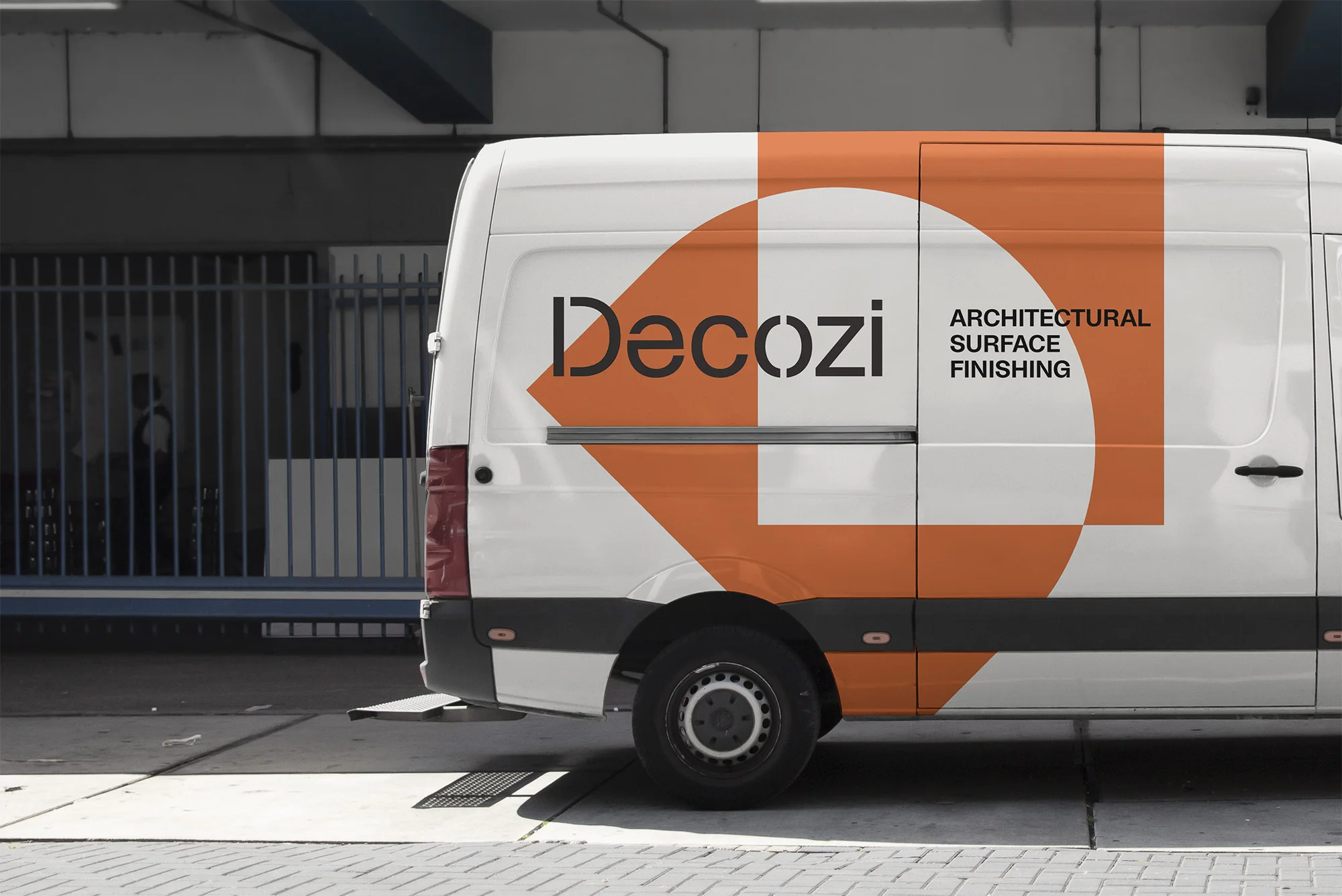 Commercial van with white exterior and orange geometric logo, parked on a paved surface in an urban setting.