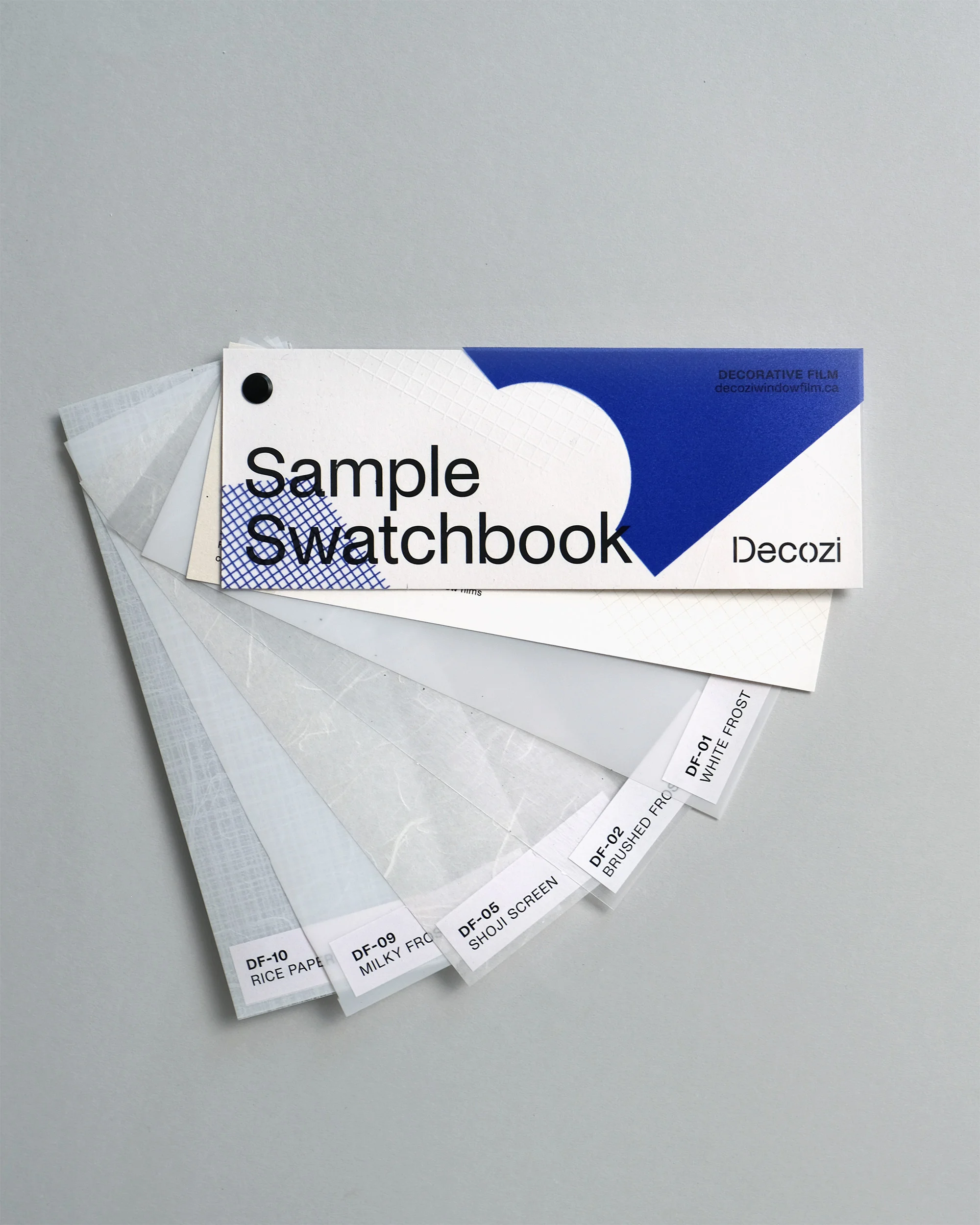A swatchbook of decorative films is fanned open on a gray surface, featuring transparent film samples with labeled product information.