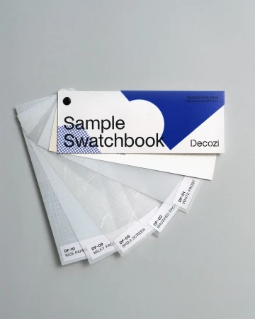A swatchbook of decorative films is fanned open on a gray surface, featuring transparent film samples with labeled product information.