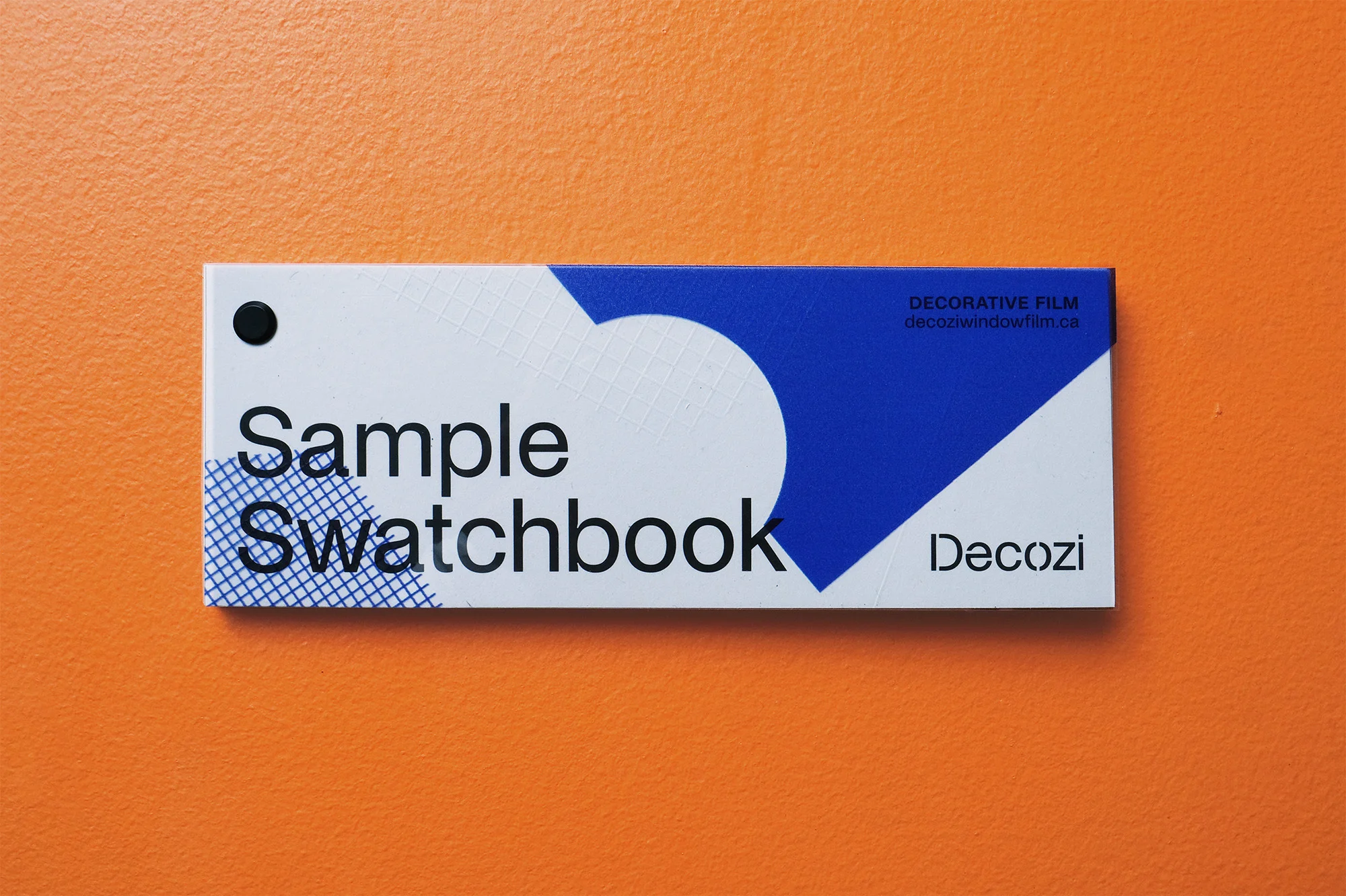 Close-up of a Decozi sample swatchbook with a white, blue, and black color scheme set against a plain orange background.