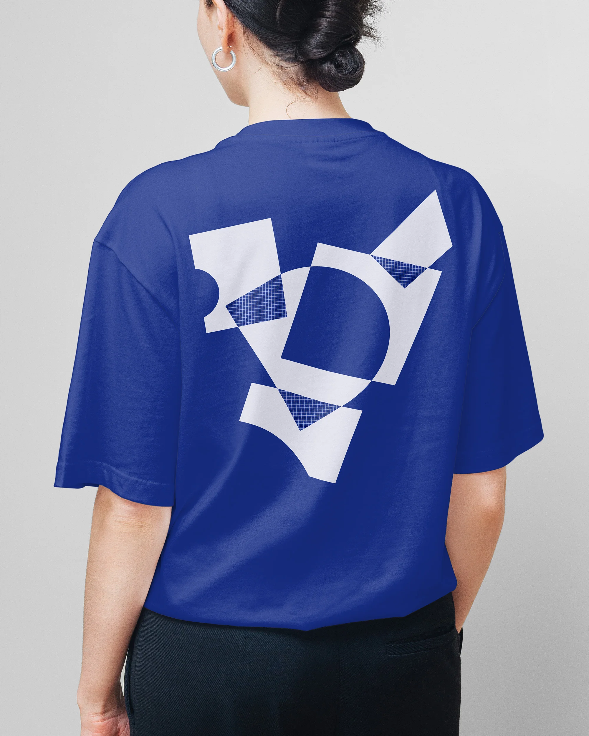 Back view of a person in a blue t-shirt featuring a white geometric design, paired with black pants against a light grey background.