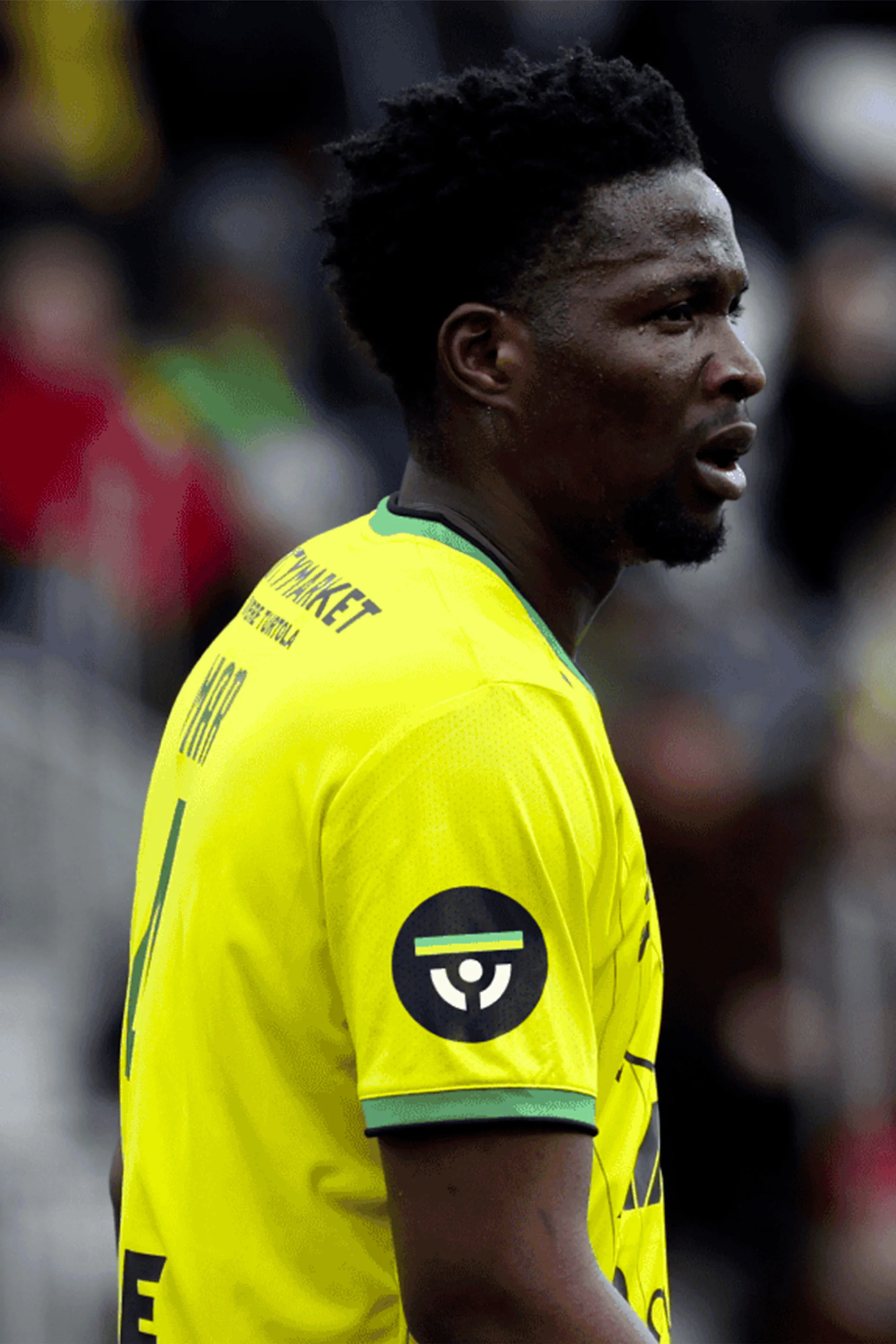 Close up of a soccer player in a bright yellow jersey with dark hair, facing sideways on an outdoor field.