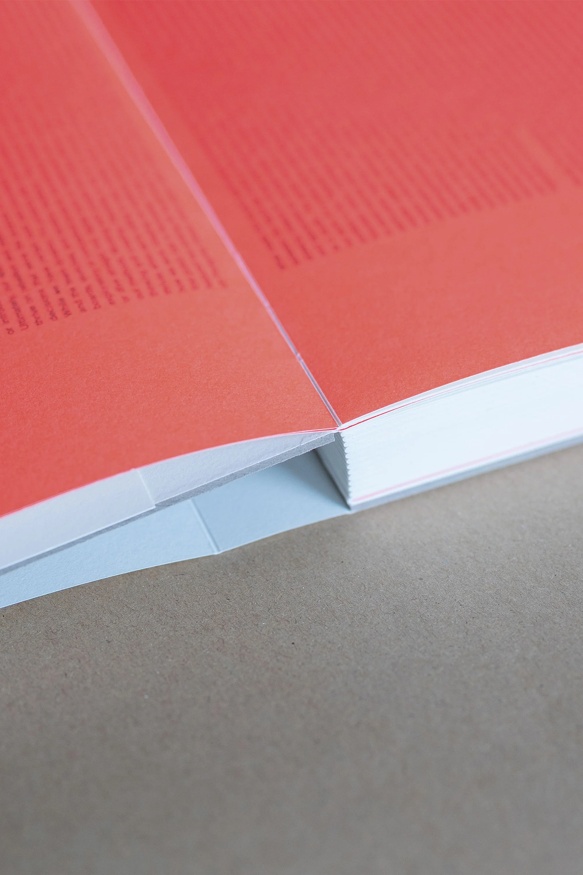 Open book with red pages and white binding, lying on a neutral-colored surface, capturing a minimalist and clean aesthetic.