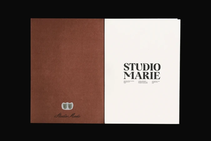 Open brochure featuring a solid brown textured cover on the left and a white page with bold Studio Marie typography on the right