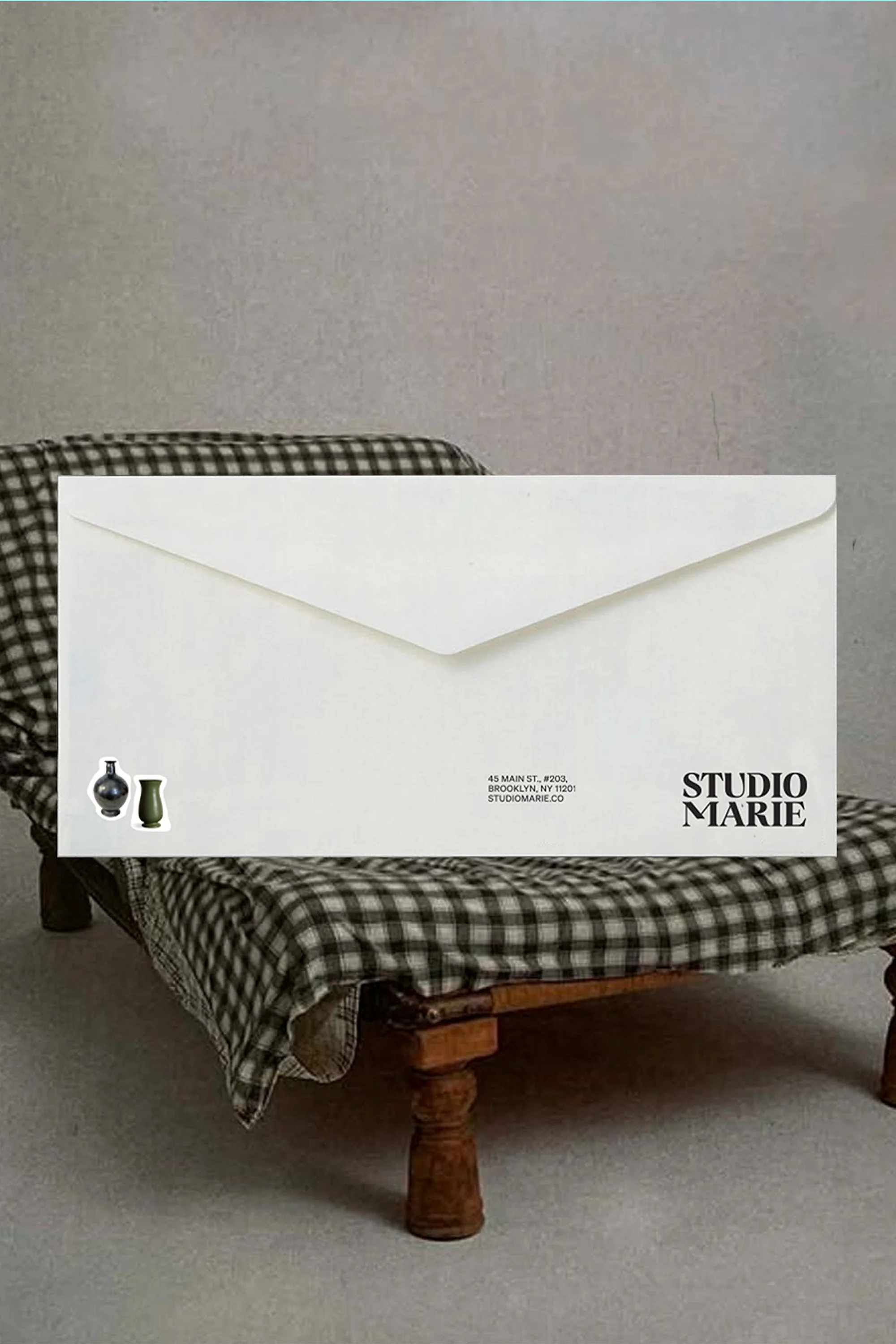 Envelope featuring Studio Marie logo on miniature settee with a checkered blanket against a neutral backdrop.