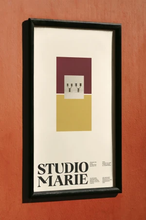 Framed art print with geometric shapes, including a burgundy square, yellow rectangle, and pair of objects, hanging on an orange wall.