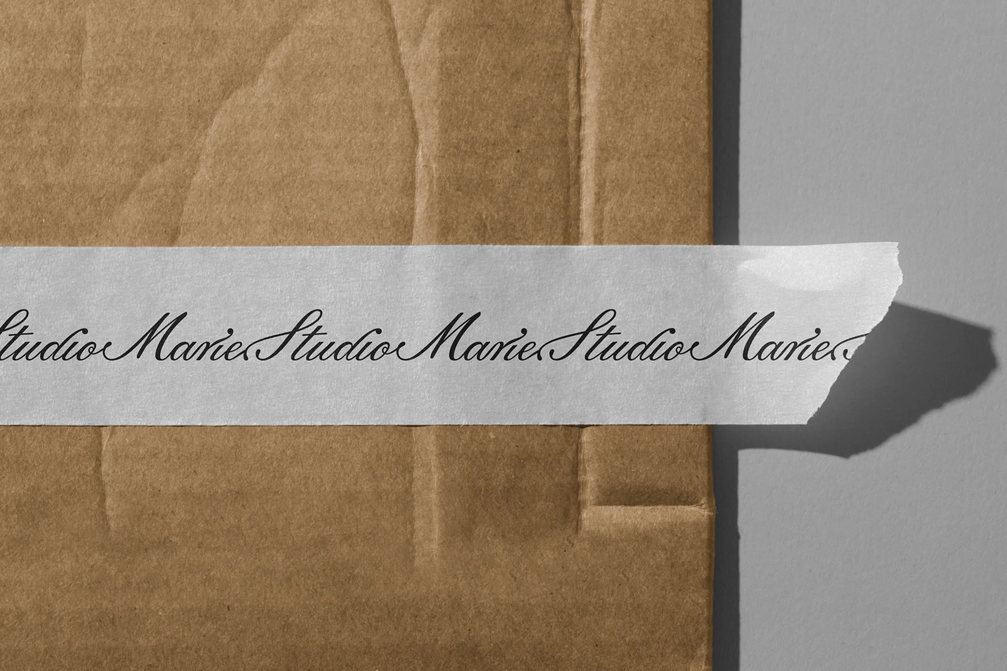 Close-up of a tan shipping envelope sealed with a label featuring stylized black cursive text 'Studio Marie' against a gray background.