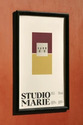 Framed poster with bold serif text reading Studio Marie mounted on an orange textured wall.
