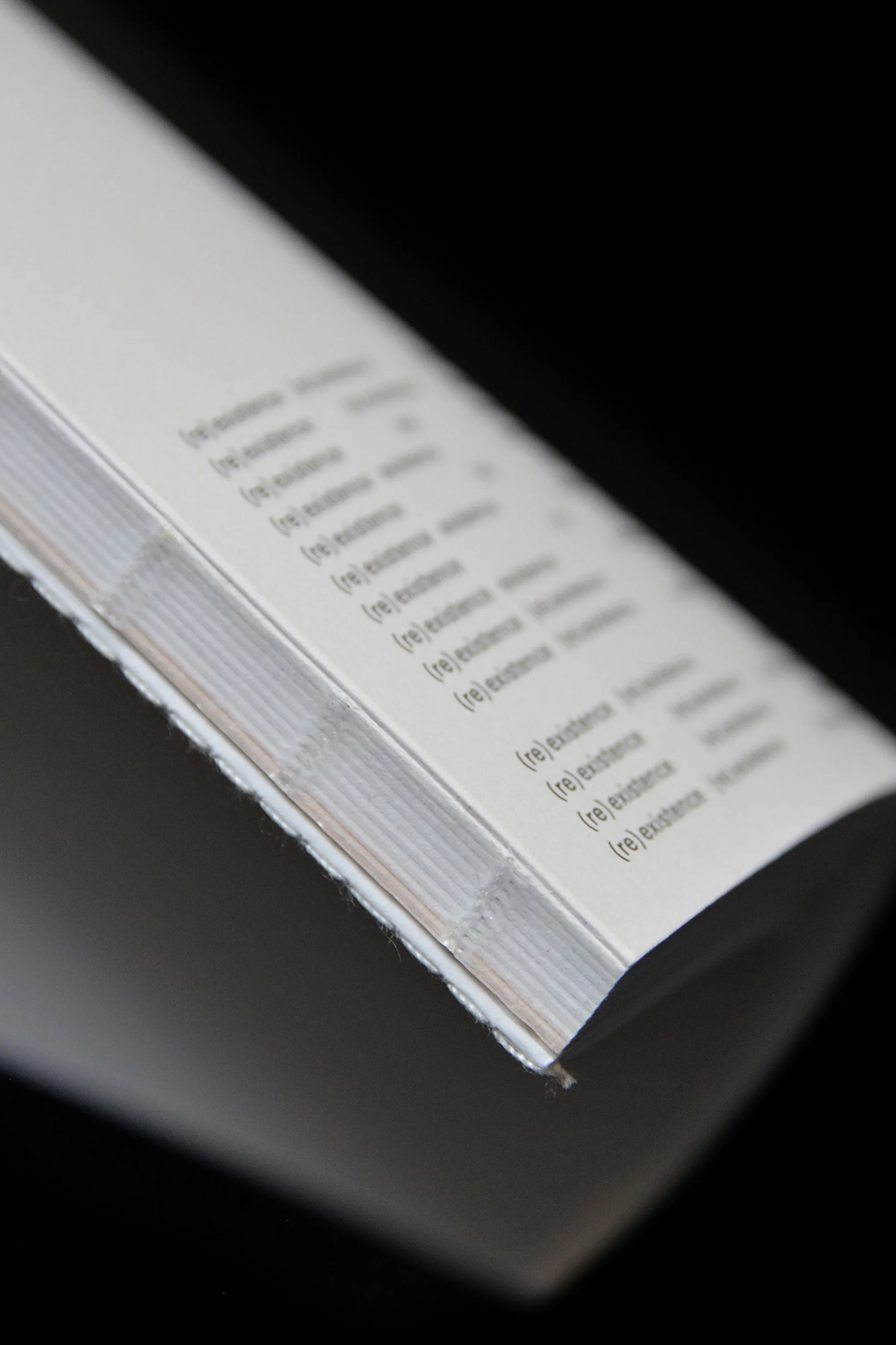 Close-up angled shot of a bound publication showing repeating black typography on white paper against a black background