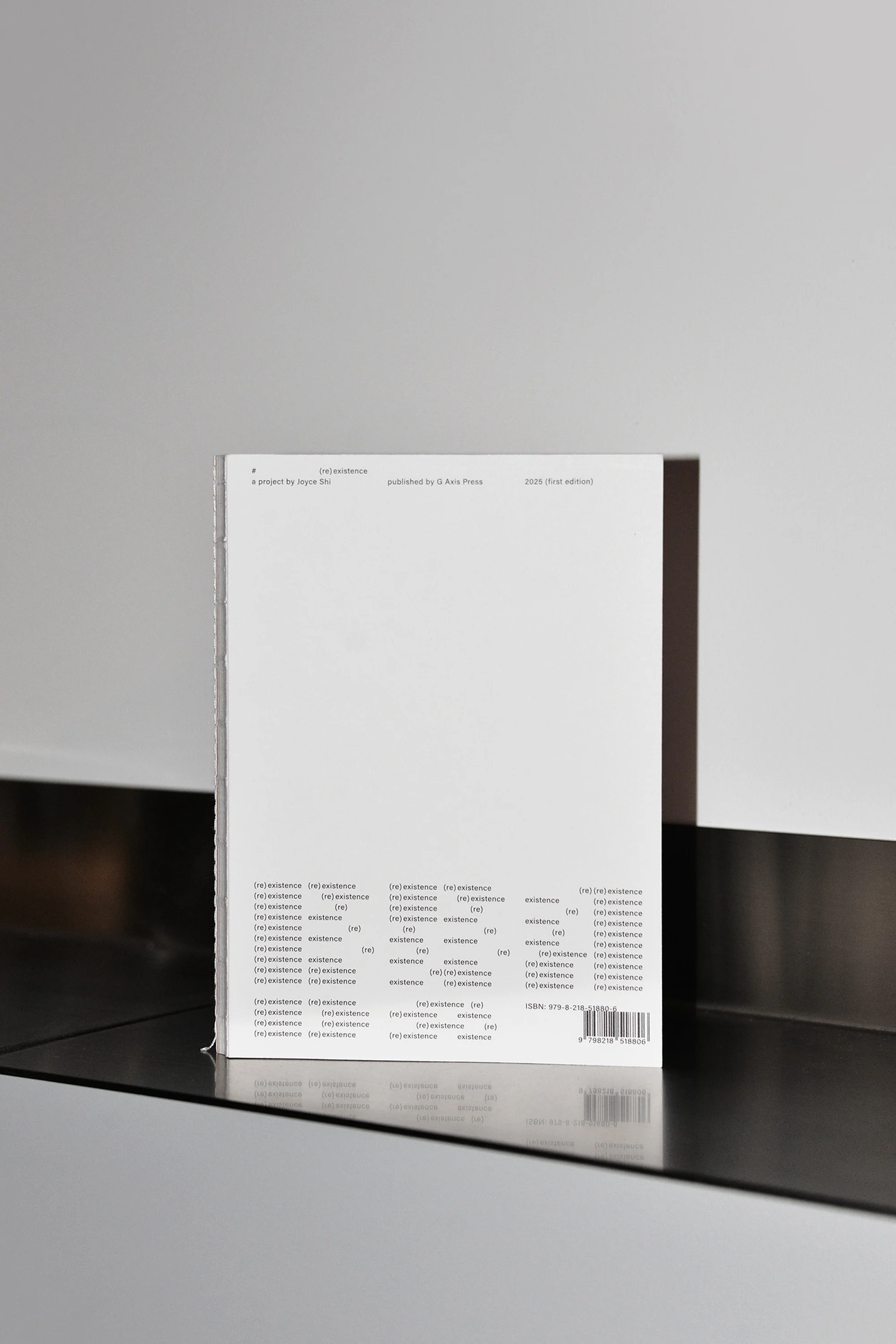 Clean product shot of a white book cover with black typography on a reflective black surface against a white and grey wall.