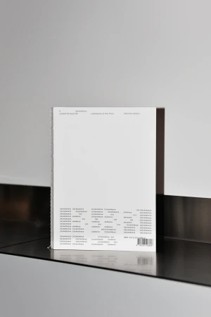 Clean product shot of a white book cover with black typography on a reflective black surface against a white and grey wall.