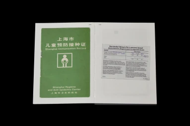 An open booklet displaying a green Shanghai Immunization Record document next to a reminder sticker on a white background.