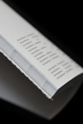 Close-up angled shot of a bound publication showing repeating black typography on white paper against a black background