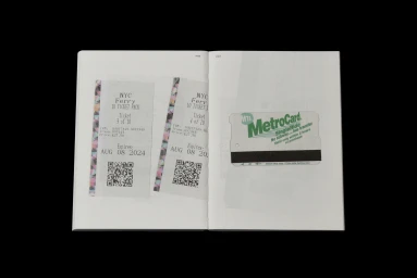 An open book displaying printed pages featuring images of NYC ferry tickets and a green MTA MetroCard.