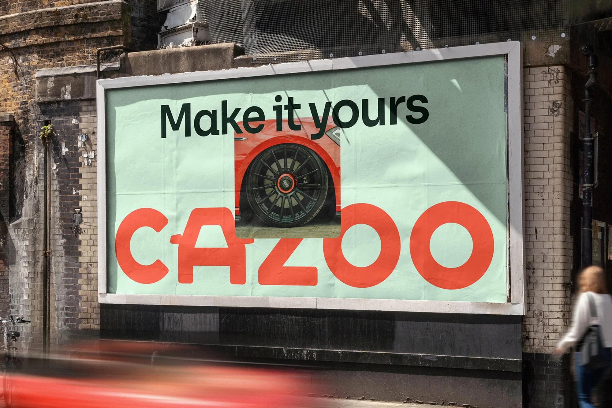 Outdoor billboard advertisement displays a red car tire and the brand name 'Cazoo' in red lettering, along with the slogan 'Make it yours'.