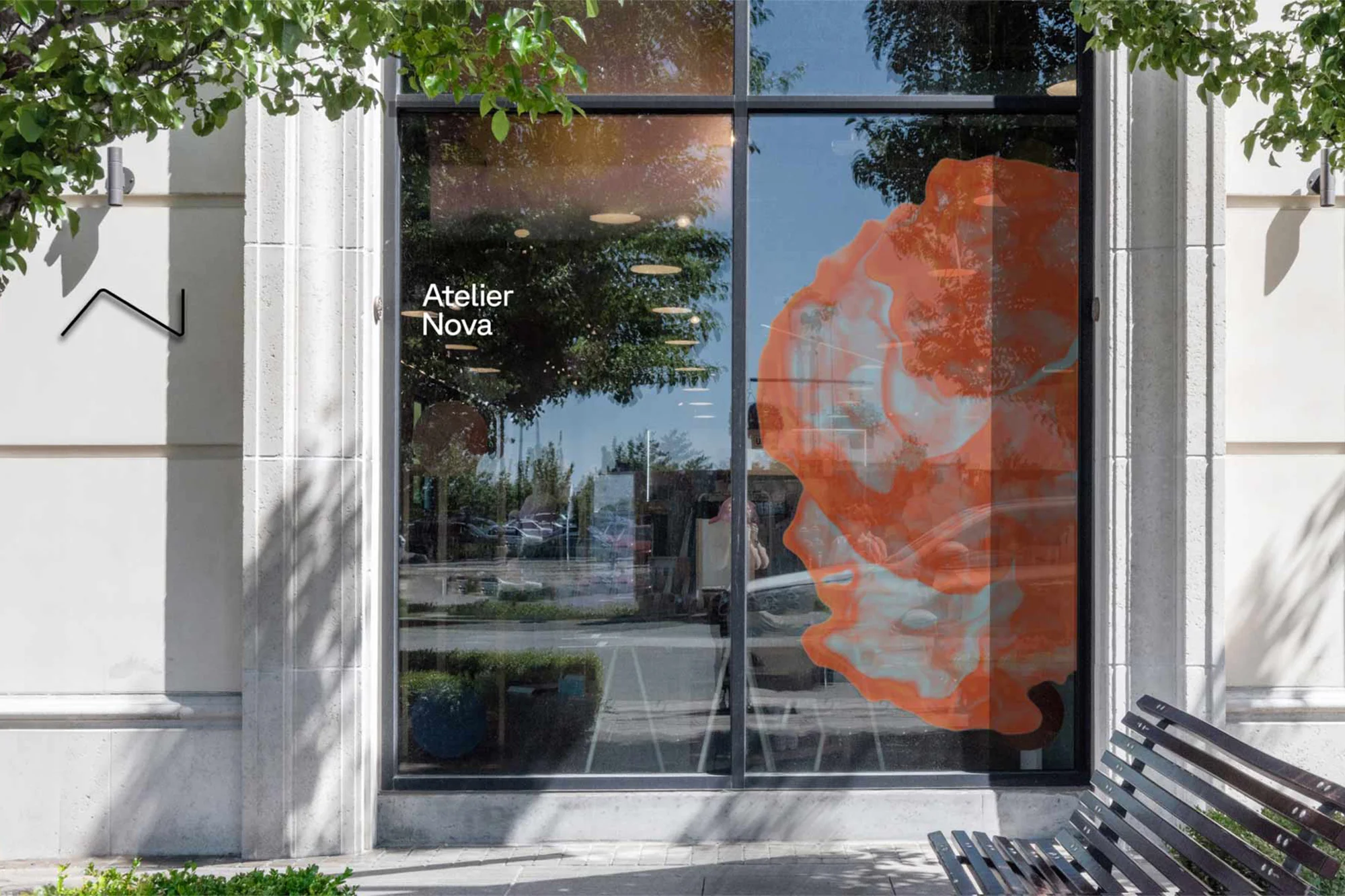 Storefront of Atelier Nova with an abstract design on the window and a bench visible in the foreground on a sunny day.