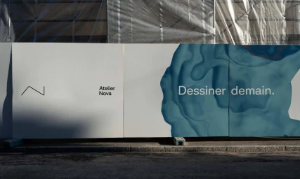 Branded construction hoarding displaying Atelier Nova logo and the text Dessiner demain against an abstract blue fluid graphic.