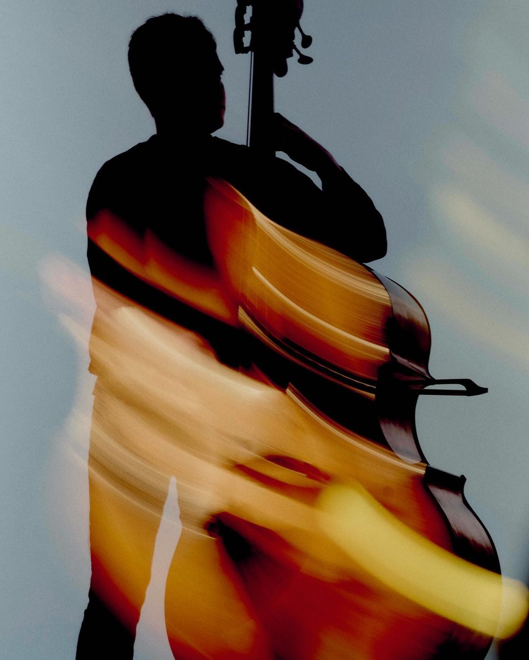 Silhouette of a person playing the double bass, motion blur effect. Musical instrument with a dark figure against a light backdrop.