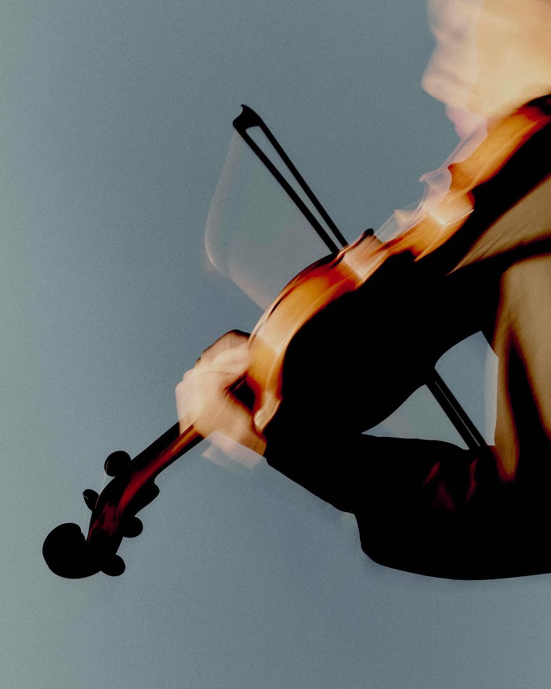 Violin player in motion with blurred effect against a gray backdrop, showcasing musical performance and artistic photography techniques.