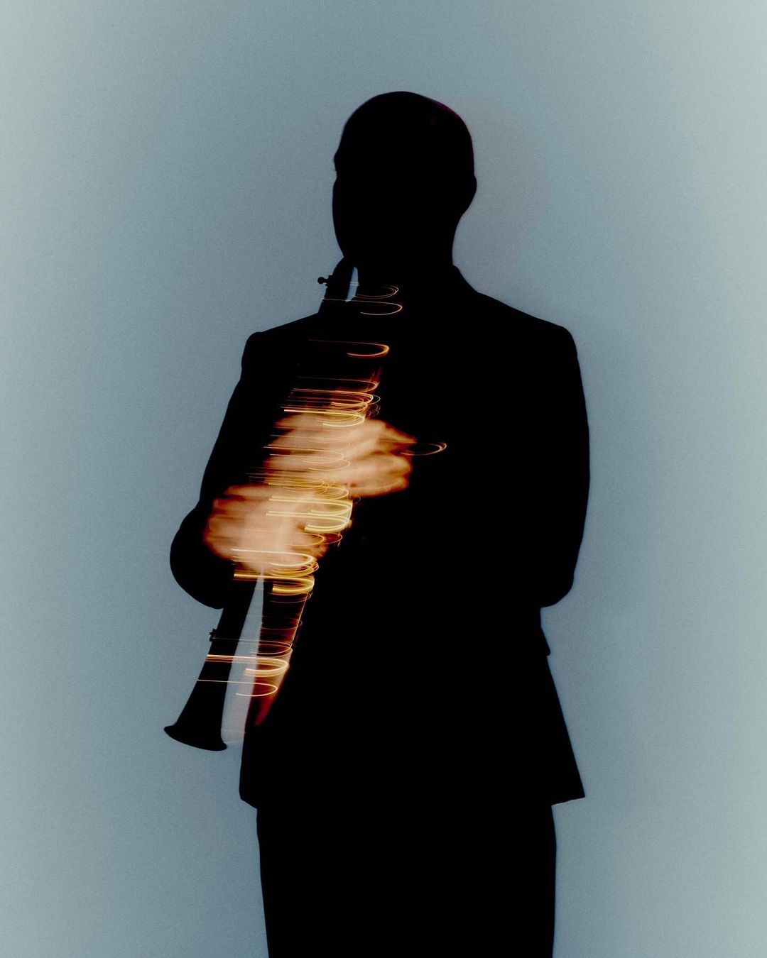Silhouette of a musician in a dark suit playing a clarinet against a light blue background with motion blur effects.