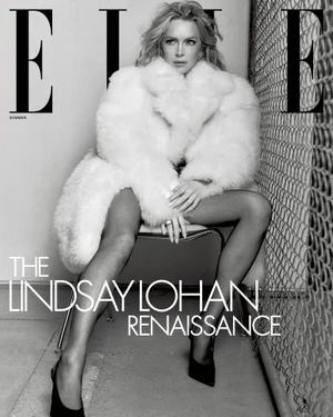 Lindsay Lohan wearing a fluffy white coat and black heels seated on a chair against chain link fencing for Elle U.S. magazine.