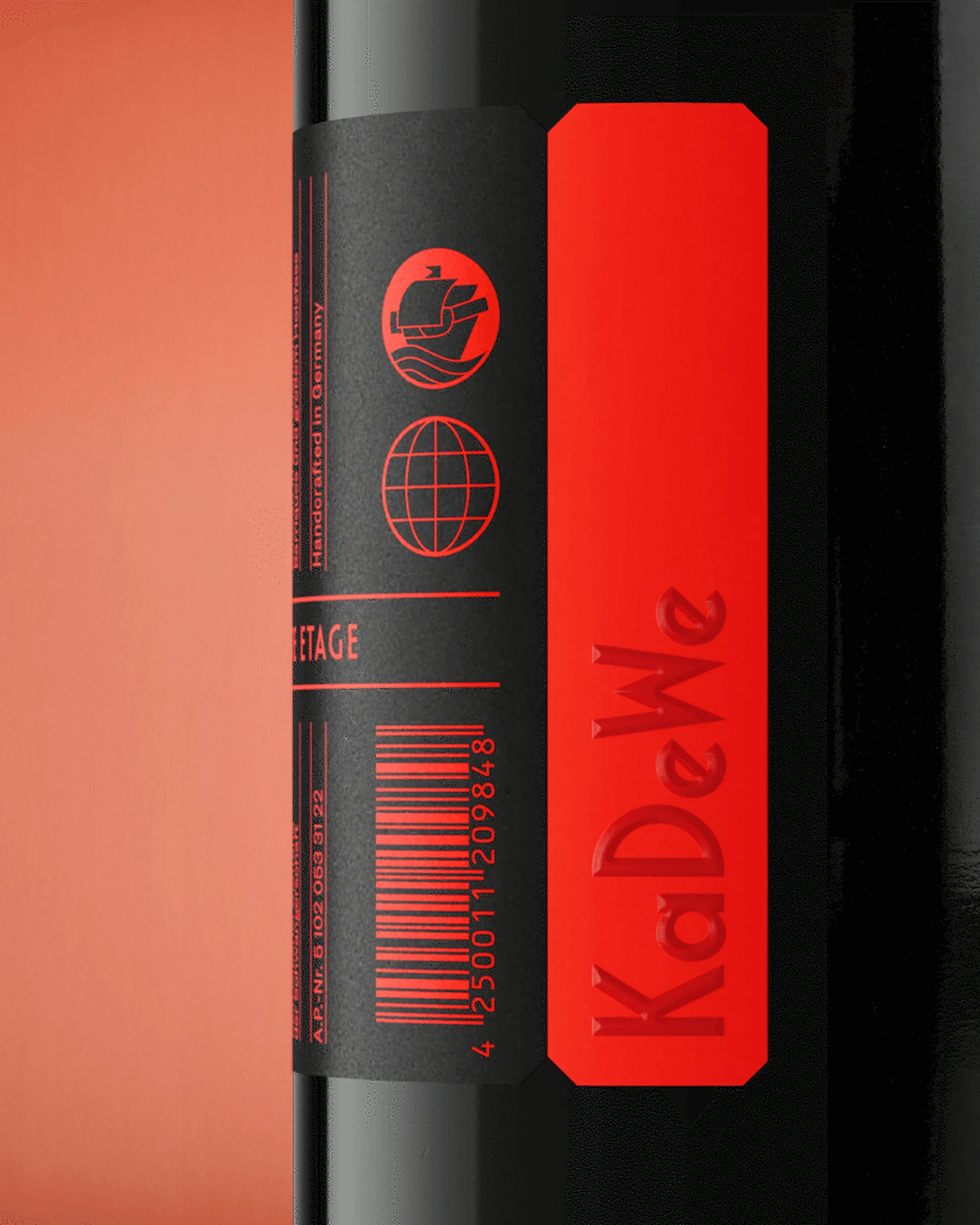 Close-up studio shot of a black bottle with a red label featuring the text 'KaDeWe', barcode, and ship logo on a peach-colored background.