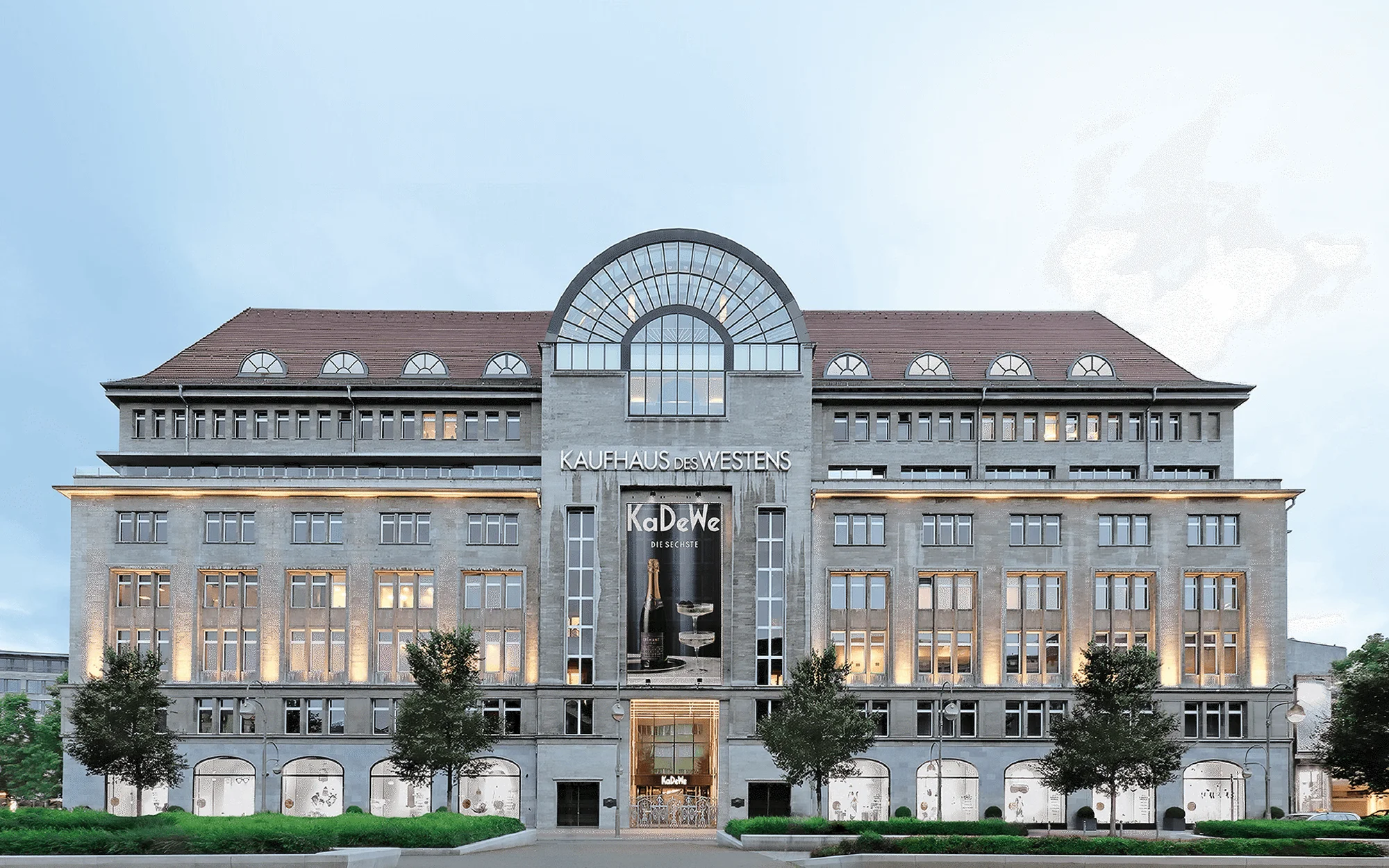 Exterior view of the KaDeWe department store in Berlin, Germany, featuring its multi-story facade, windows, signage, and street-level greenery.