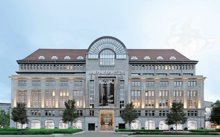 Exterior view of the KaDeWe department store in Berlin, Germany, featuring its multi-story facade, windows, signage, and street-level greenery.