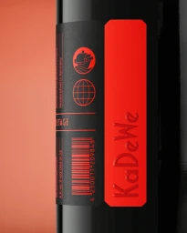 Close-up product shot of a black bottle with a black and red label featuring debossed KaDeWe text and icons against a warm peach background.