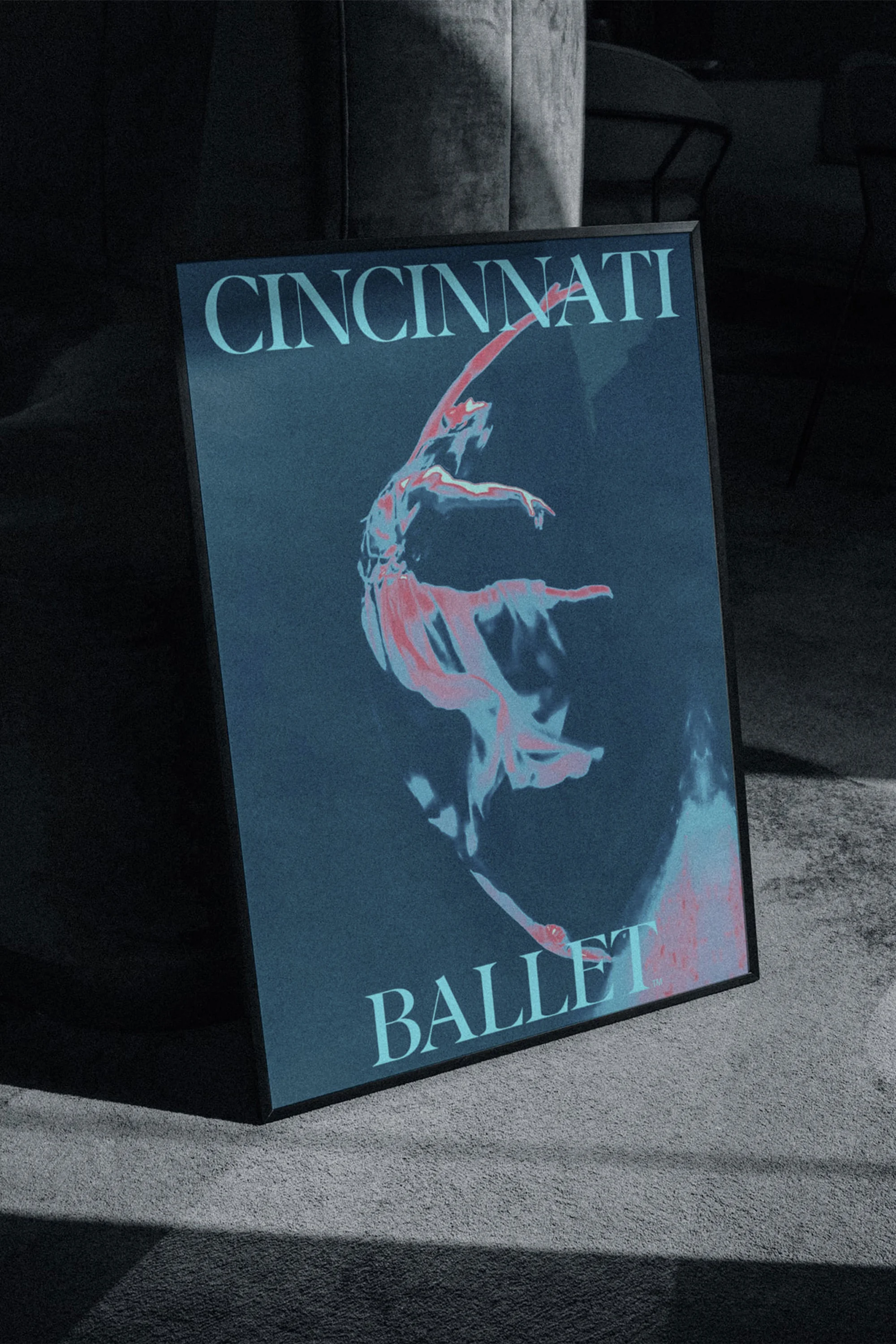 Framed poster of a ballet dancer in mid-performance, displayed indoors with text reading 'Cincinnati Ballet' against a dark blue backdrop.