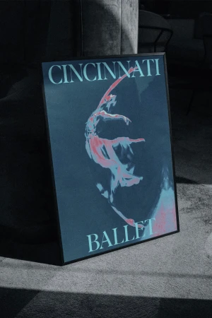 Framed poster of a ballet dancer in mid-performance, displayed indoors with text reading 'Cincinnati Ballet' against a dark blue backdrop.