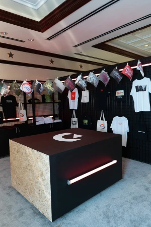 An interior product shot showcasing a display with hanging flags, t-shirts, and tote bags against a black wall with stars.