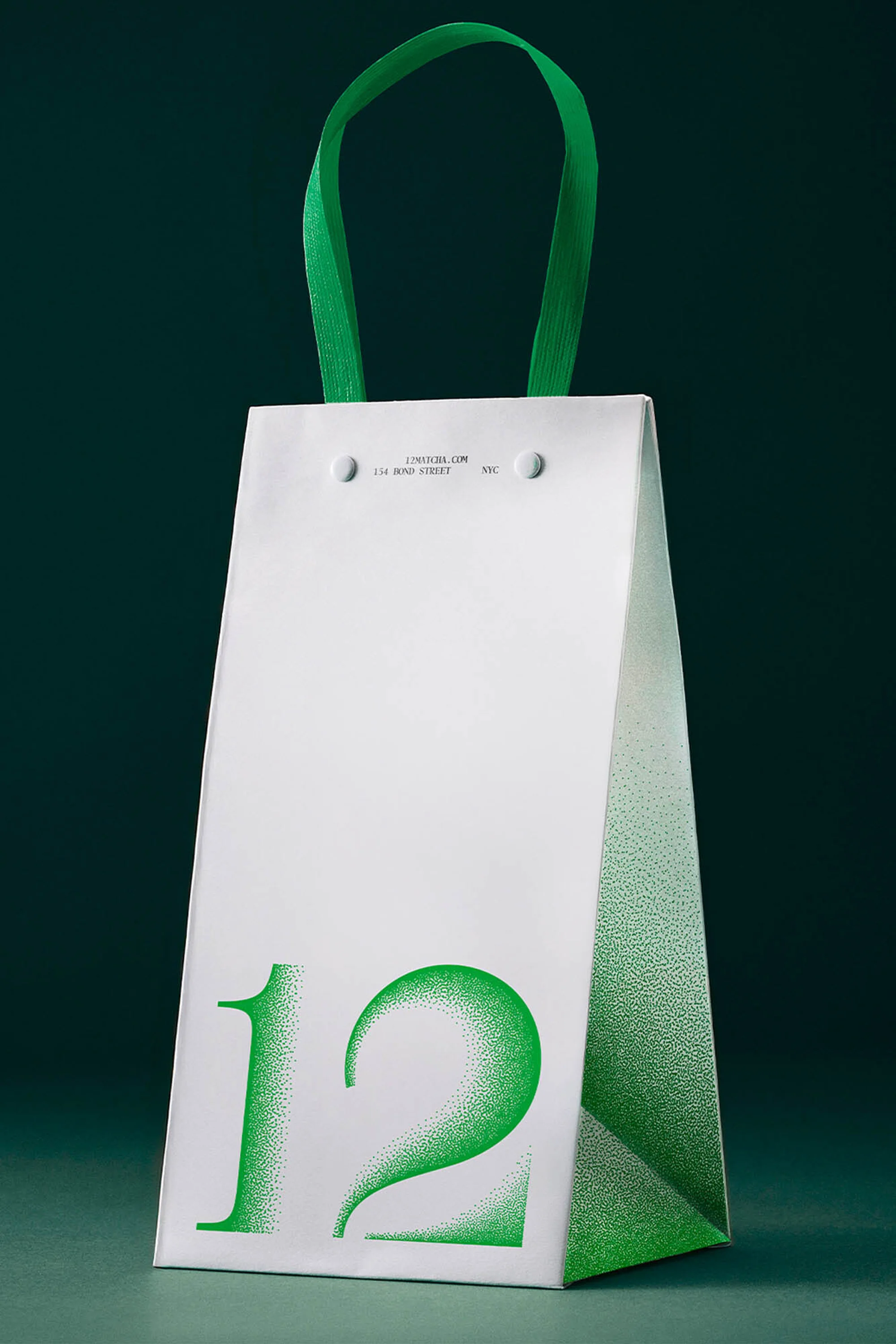 White paper gift bag with green handle and number twelve design element against a solid dark green background.
