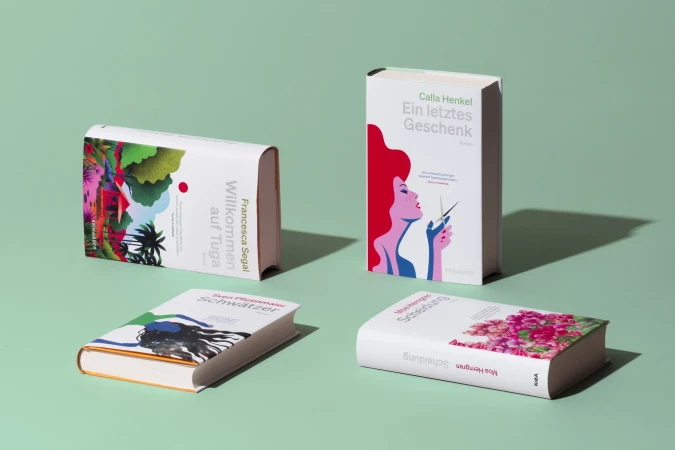 Four white hardcover books with colorful illustrations on a light green background, showcasing graphic design in a studio setting.