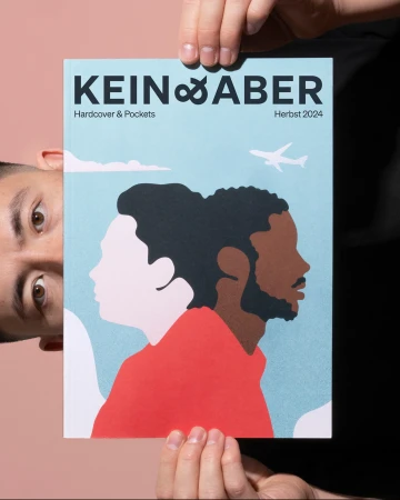 Person holding a book cover with abstract illustrations of human profiles in front of a split pink and black background.