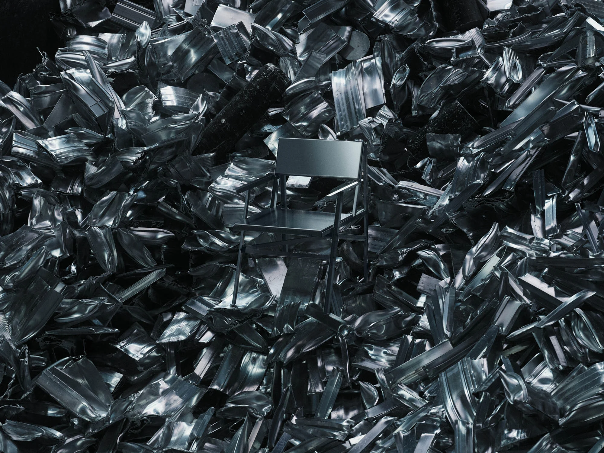 Elevated view of a chair surrounded by crushed silver metal sheeting and metal fragments, studio lighting, metallic reflections.