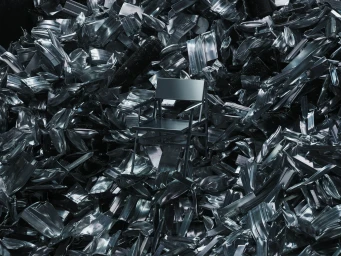 A sleek dark metal chair placed centrally amidst a massive heap of crushed and crumpled metallic scrap waste.