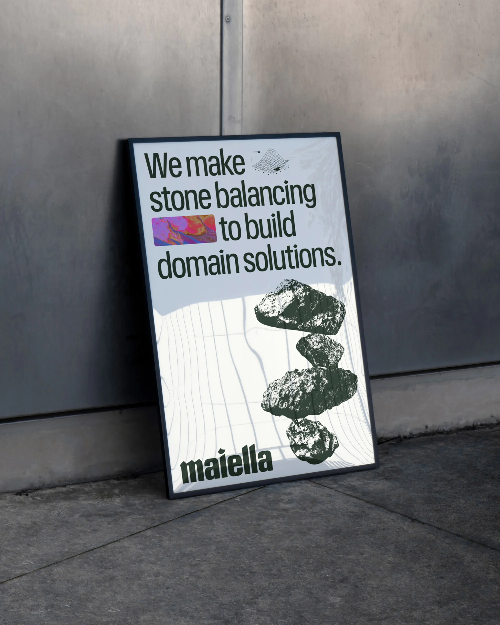 Framed poster on a grey floor against a grey wall, featuring stacked stones graphic and text 'We make stone balancing to build domain solutions'.