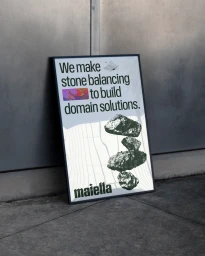 A framed graphic poster leaning against a concrete wall displaying stacked stones and typography for Maiella.